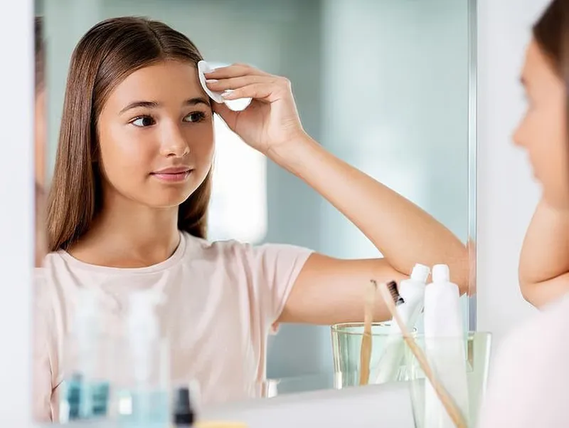 تصویر دختری نوجوان روبروی آینه در حال پاک کردن صورت